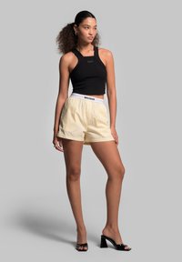 Black ribbed crop top with a round neckline, paired with light yellow striped shorts featuring a white elastic waistband. Black heeled sandals.