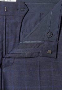 Pantalon bleu marine à motif carreaux, avec fermeture éclair, bouton et poches latérales. Le tissu a une texture lisse.