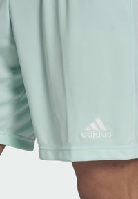 Licht mintgroene sportshorts gemaakt van gladde stof, met een geborduurd wit Adidas-logo aan de linkeronderzijde.