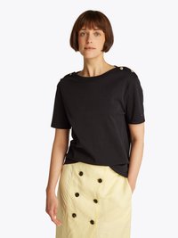 Black short-sleeved t-shirt with a round neckline and golden button accents on the shoulder, paired with a light yellow skirt featuring black buttons.