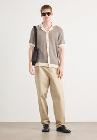 Short-sleeve knit shirt in brown and cream, with button front and collar; paired with beige pants and black shoes. Accessory: black shoulder bag.