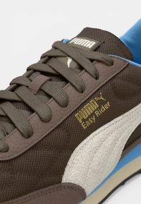 Braune und beige Puma Easy Rider Sneaker mit braunen Schnürsenkeln und blauer Innenausstattung, die Branding und strukturierte Stoffe zeigt.