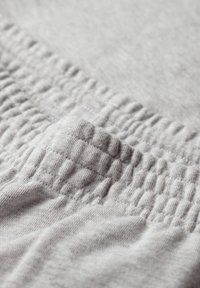 Tela gris claro con una cinturilla elástica texturizada. El material es suave con un aspecto ligeramente jaspeado, exhibiendo detalles de costura sutiles.