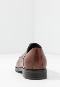 Chaussure en cuir marron avec une finition lisse, bout arrondi et semelle en caoutchouc noire. Comprend des détails de couture subtils et un petit talon.