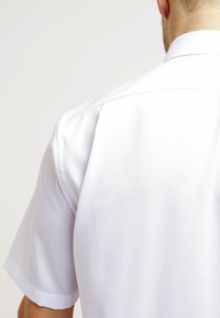 Camicia bianca a maniche corte con una texture liscia, dotata di un colletto classico e cuciture pulite. Nessun motivo visibile o dettagli metallici.