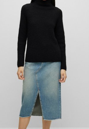 Femme portant un pull à col roulé noir associé à une jupe midi en denim bleu clair avec une fente avant et un ourlet brut.