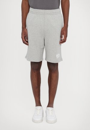 Gray cotton shorts with an elastic waistband, side pockets, and a printed logo on the lower hem. Styled with white sneakers.