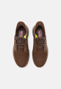 Barna, slip-on stílusú cipők hálós és bőr felsőrésszel, textúrált felülettel, sima talppal, és színes belső béléssel, sárga kiegészítőkkel.
