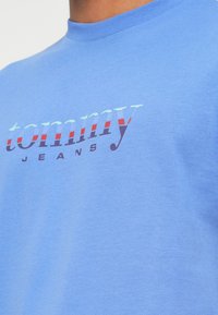 Modra bombažna majica s kratkimi rokavi, na kateri je napisan "tommy JEANS" v večbarvnih črkah, z okroglim ovratnikom in standardnim krojem.