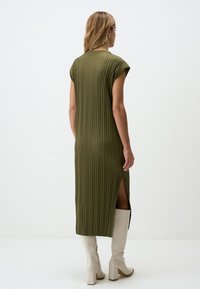 Abito midi a pieghe verde con maniche corte, caratterizzato da uno spacco laterale, abbinato a stivali beige con tacco quadrato al ginocchio. Tessuto morbido.