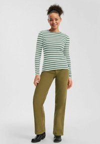 Haut à manches longues rayé vert et blanc associé à un pantalon texturé vert olive et des bottines noires. Design simple avec texture côtelée.