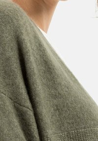 Olivengrøn sweater lavet af blødt strikmateriale med en afslappet pasform og dropped shoulder-design, der har en subtil tekstur.
