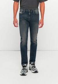 Mørkeblå denimbukser med slim fit, med knapp og glidelås, frontlommer og subtil falming. Kombinert med grå joggesko.