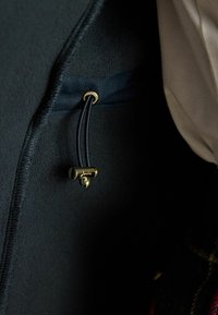 Schwarzes Fleece-Innenfutter mit einem goldenen Hardware-Verschluss und einem dunklen Band, das in einer Tasche platziert ist, im Kontrast zu einem hellen Stoff.