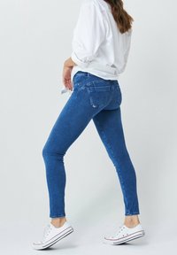 Modré skinny džíny, denimová tkanina, střední praní, pět kapes, šité detaily, zkombinované s bílými teniskami a volnou bílou košilí.