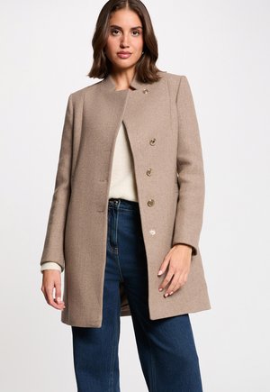 Beige uldblandingsfrakke med lige snit, der har høj krave, fem knapper i guldfarve og sidelommer, parret med vide jeans.