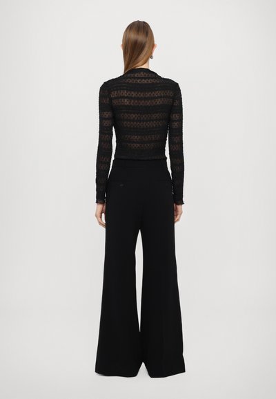 Zwart doorschijnend lange mouwen top met gestreepte patronen. Losse zwarte broek met brede pijpen, hoge taille en achterzakken.