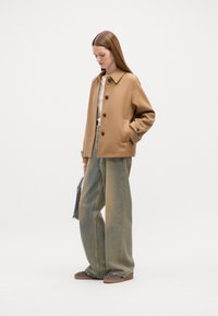 Afslappet beige jakkesæt med knapper, båret over en lys top og parret med løse, lyse denim jeans. Accentueret med en sort-hvid stribet taske.