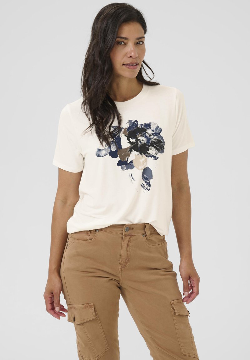 Cremefarbenes T-Shirt mit kurzen Ärmeln und einem navyfarbenen Blumenprint in der Mitte, kombiniert mit khakifarbenen Cargo-Hosen mit Seitentaschen. Weicher Stoff, lockere Passform.