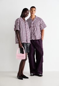 Camisas às riscas em roxo e branco, uma bolsa de pérolas rosa, calções de pele e calças roxas largas. Texturas únicas e designs de corte solto.