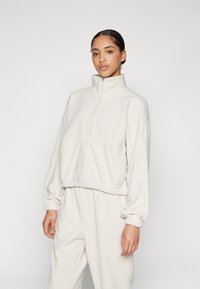 Light beige fleece pullover with a high collar, front zip, elastic cuffs, and hem; features subtle Nike logo on the chest.