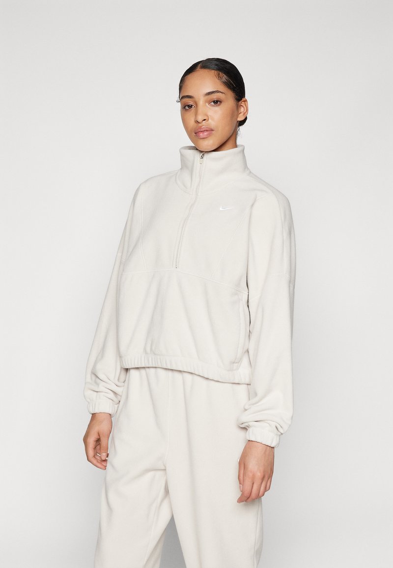 Light beige fleece pullover with a high collar, front zip, elastic cuffs, and hem; features subtle Nike logo on the chest.