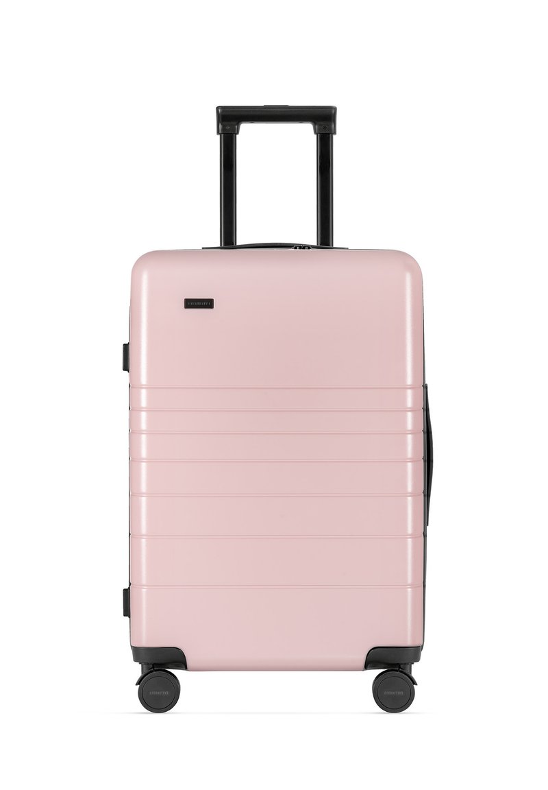 Różowa, twarda walizka o eleganckim designie, z poziomymi liniami, teleskopową czarną rączką oraz obrotowymi kółkami ułatwiającymi mobilność.