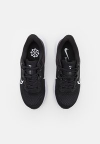 Zwarte sportieve schoenen met een mesh bovenkant, contrasterend wit swoosh-logo en een gewatteerde witte zool. Voorzien van een traditionele vetersluiting.