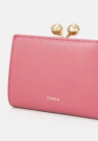 Furla novčanik od mekog ružičastog kože s zlatnim detaljima, s kopčom za zatvaranje i utisnutim logotipom na prednjoj strani. Glatka tekstura i pravokutni dizajn.