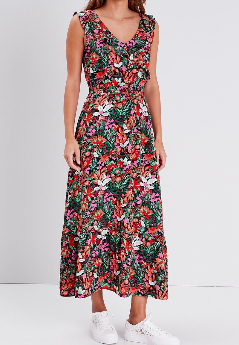 Robe sans manches à motifs floraux rouges, roses, blancs et verts portée avec des baskets blanches par une femme debout.