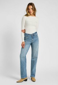 Maglione bianco a coste con maniche lunghe abbinato a jeans a gamba larga blu chiaro e mule beige. Il maglione presenta un collo a barca e una vestibilità slim.