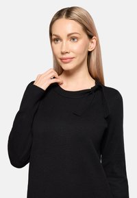 Schwarzer Strickpullover mit langen Ärmeln, runden Ausschnitt und einer dekorativen Schleifendetail am Kragen. Glatte Textur.