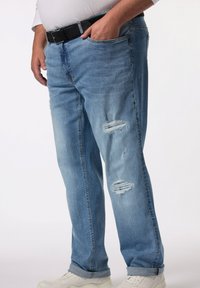 Vaqueros de mezclilla azul claro con un corte relajado, que presentan parches desgastados en los muslos y puños doblados. Combinados con zapatillas blancas.