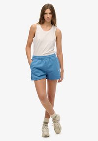 Niebieskie bawełniane szorty z postrzępionym dołem, elastycznym pasem i bocznymi kieszeniami, zestawione z beżowym topem na ramiączkach i jasnymi sneakersami.