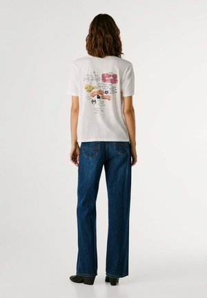 T-shirt en coton blanc avec un texte graphique multicolore au dos. Associé à un jean bleu à jambes larges et des bottes à talons noires.