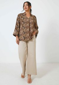 Brown snake print shirt with a loose fit, collared neckline, and three-quarter sleeves, paired with beige wide-leg trousers and clear sandals.