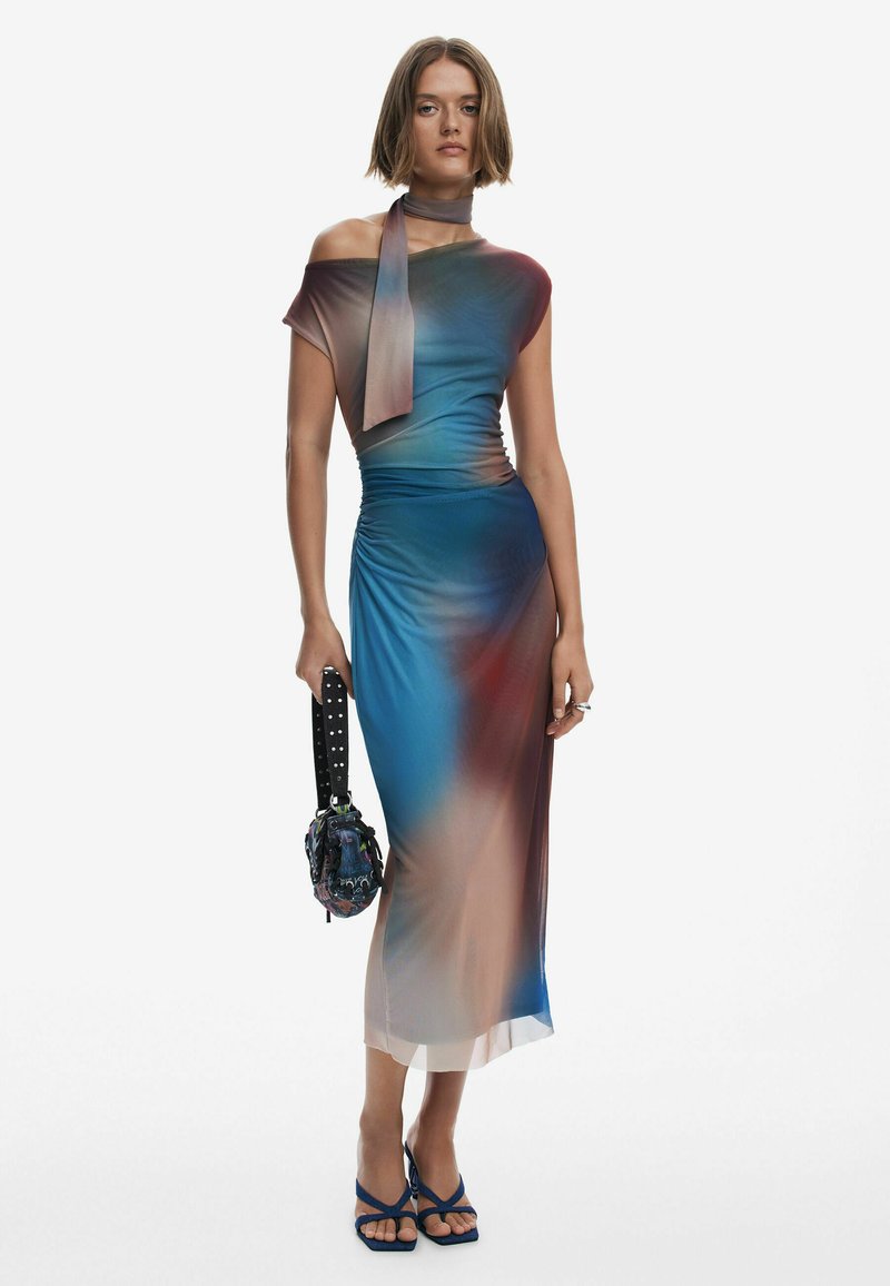 Langes, figurbetontes Kleid in Farbverläufen von Blau und Braun, mit einem schulterfreien Design und einem passenden Schal. Begleitet von einer gemusterten Handtasche.