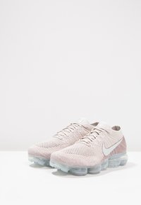 Lichtroze Nike Air Max schoenen met een gebreide bovenkant, een gestructureerd patroon en een transparante luchtgepolsterde zool. Iconisch wit swoosh-detail.