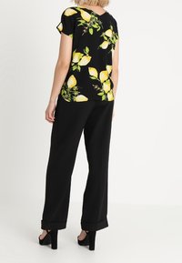 Top negro de manga corta con estampado de limones amarillos, combinado con pantalones negros holgados. El conjunto presenta un ajuste relajado y una textura suave.