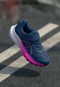 Blue athletic shoe with pink accents and a textured upper, featuring a velcro strap and cushioned white sole.