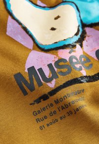 Tessuto marrone con design grafico multicolore con accenti rosa, blu e crema. Testo: "Musée", "Galerie Monbmaître" e date.