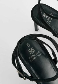 Sandali neri con tacco alto e più cinturini in pelle liscia, con un logo discreto e le informazioni sulla taglia sulla soletta.
