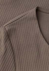 Tessuto a coste marrone che mette in mostra una morbida texture e un collo rilassato. Il materiale presenta una leggera lucentezza e diverse trame a strisce.