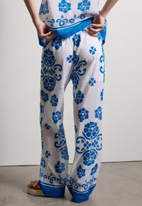 Pantalons blancs avec des motifs floraux bleus, présentant une coupe décontractée et une taille unie bleue. Portés avec un top assorti pour un look harmonieux.