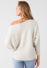 Suéter de crema claro sin mangas con textura acanalada, corte holgado y mangas caídas. Combinado con jeans azul claro.