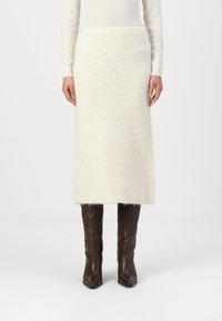 Jupe midi en tricot blanc texturé avec une coupe droite, associée à des bottines en cuir marron ajustées avec un motif décoratif.