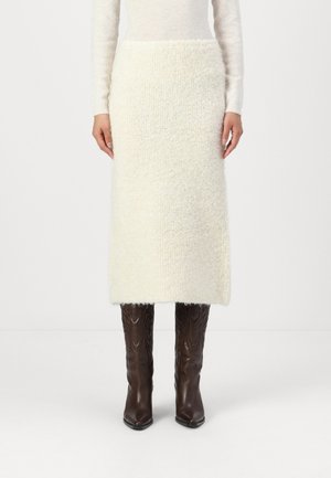Textured white knit midi skirt with a straight cut, paired with fitted brown leather ankle boots featuring a decorative pattern.
