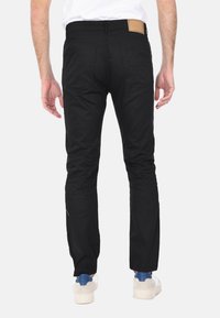 Pantaloni dritti neri con una texture liscia, dotati di tasche posteriori e una patch in pelle marrone sulla vita.
