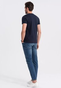 Námorně modré bavlněné tričko s krátkým rukávem a kulatým výstřihem, spárované s světlemodrými džíny a bílými botami. Pohled zezadu.