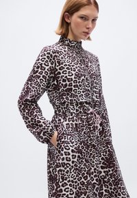 Φόρεμα με λεοπάρ σχέδιο, ψηλό γιακά, μακριά μανίκια και ελαστική μέση. Διαθέτει τσέπες και ροζ κορδόνι στο στήθος. Μαλακή υφή υφάσματος.